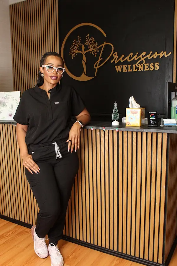 Precision Wellness team member standing at the front desk in front of the clinic’s branded reception wall.