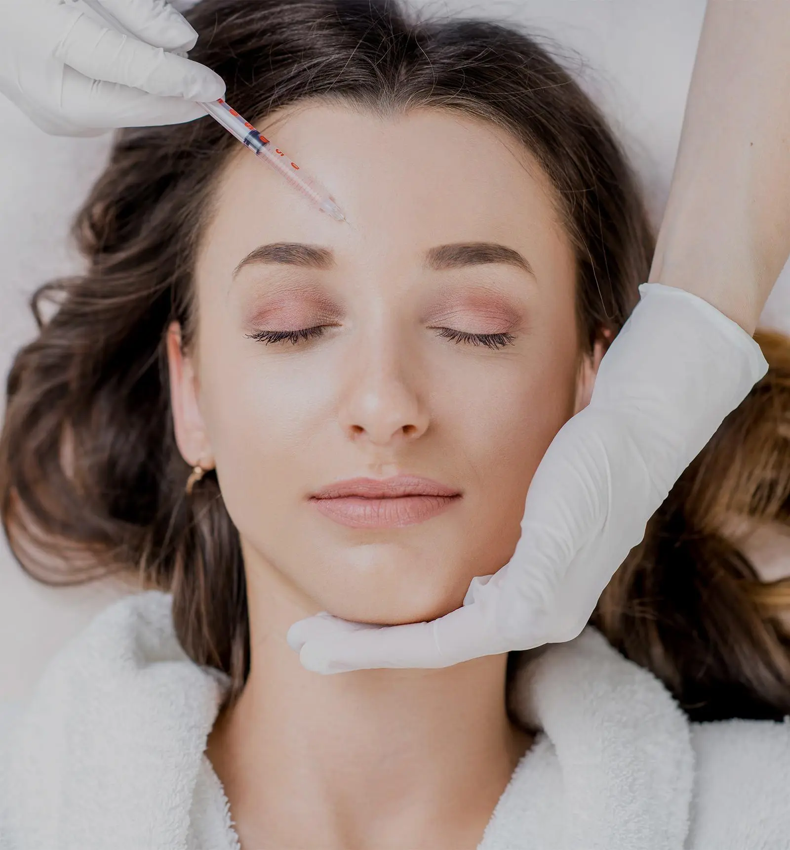 Woman with closed eyes receiving a gentle facial treatment while a skincare professional supports her face with gloved hands.