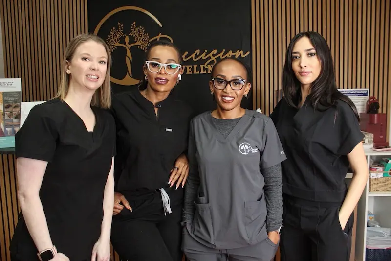 Four Precision Wellness team members standing together in front of the clinic’s branded reception wall.